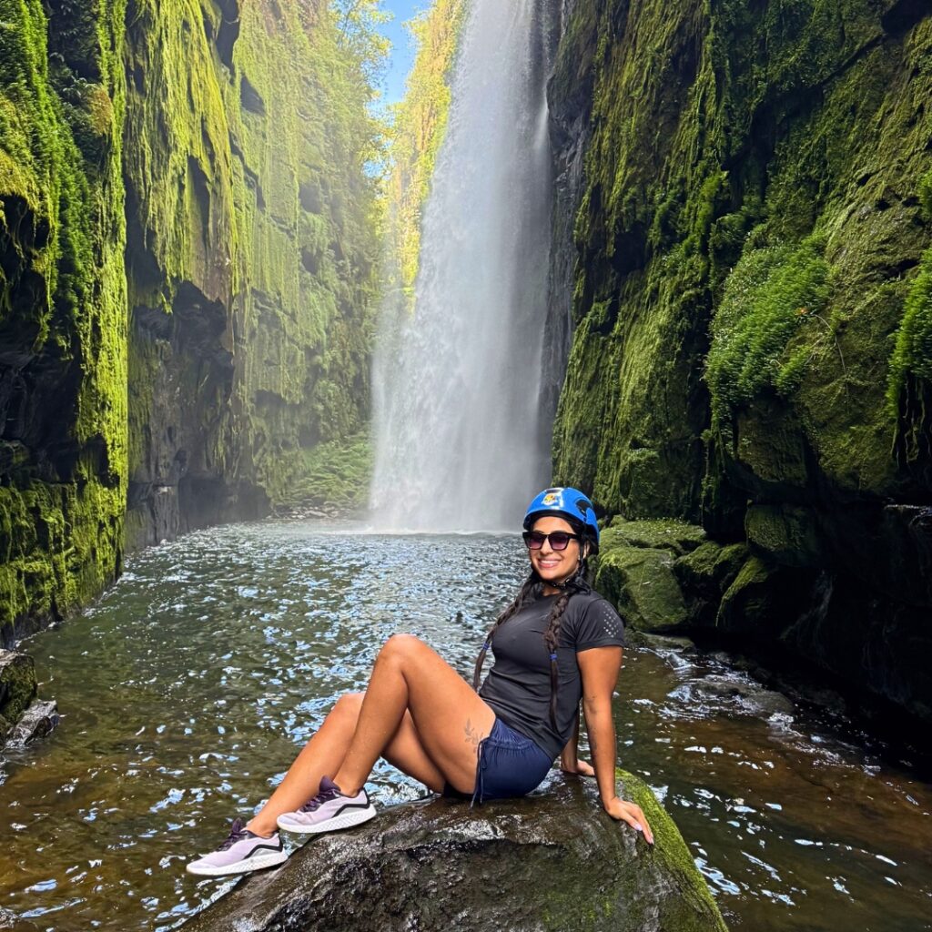 Turista com capacete de segurança sentada em pedra dentro do Cânion do Ribeirão Lajeado Grande, em frente à imponente queda da Cachoeira do Véu da Noiva em Jaguariaíva, Paraná.